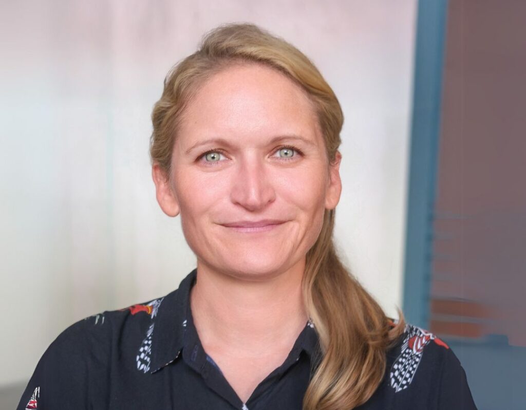 Person with long blonde hair wearing a dark patterned shirt