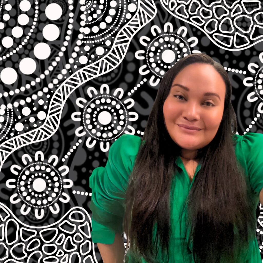 First Nations woman wearing a green shirt, standing in front of a black and white aboriginal art work