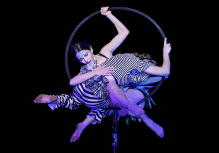 Two people in the air with a hoop, black background and purple light on them
