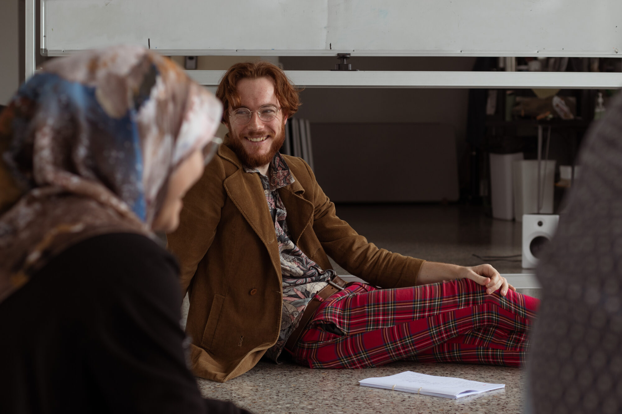 Robbie Fieldwick sitting on the ground smiling, a woman sits in the foreground blurred