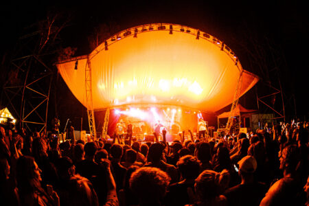 Music concert with people in foreground and yellow lit up stage in background