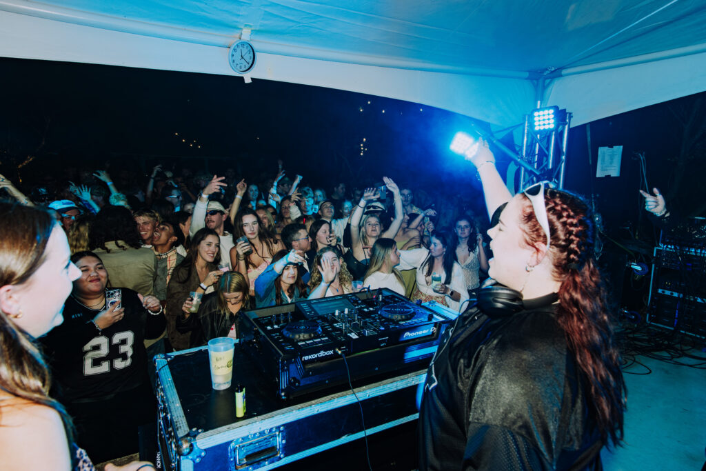 DJ RORK performing at a liveley event with crowd dancing and raised hands, lights and blurred faces create an energetic scene
