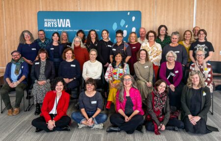 Group of people standing in front of a large blue banner at the Regional Arts Network Perth event with 19 WA orgs, including Minister for Creative Industries Simone McGurk.