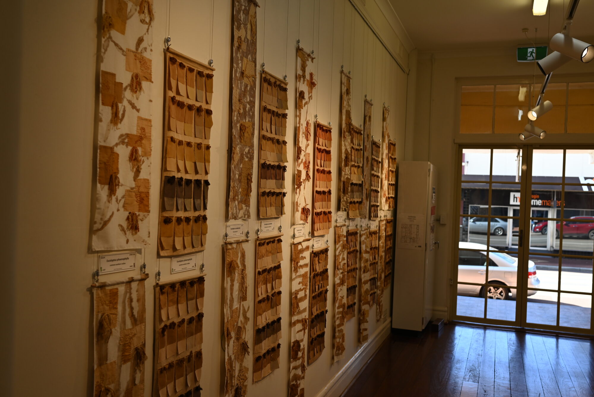 A gallery exhibition with textile swatches in various earthy-brown colours hung up on the wall.