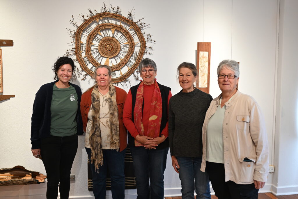 Five people posing for a group photo in an art exhibition space.