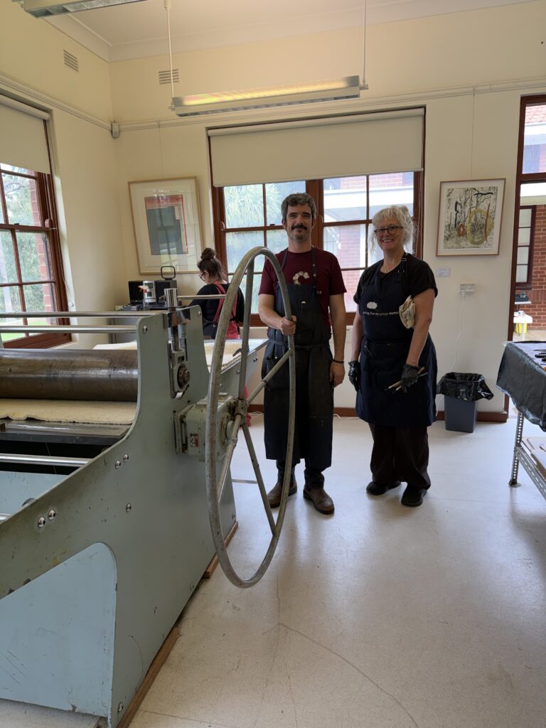 A man and a woman standing next to a prepress machine in a studio.