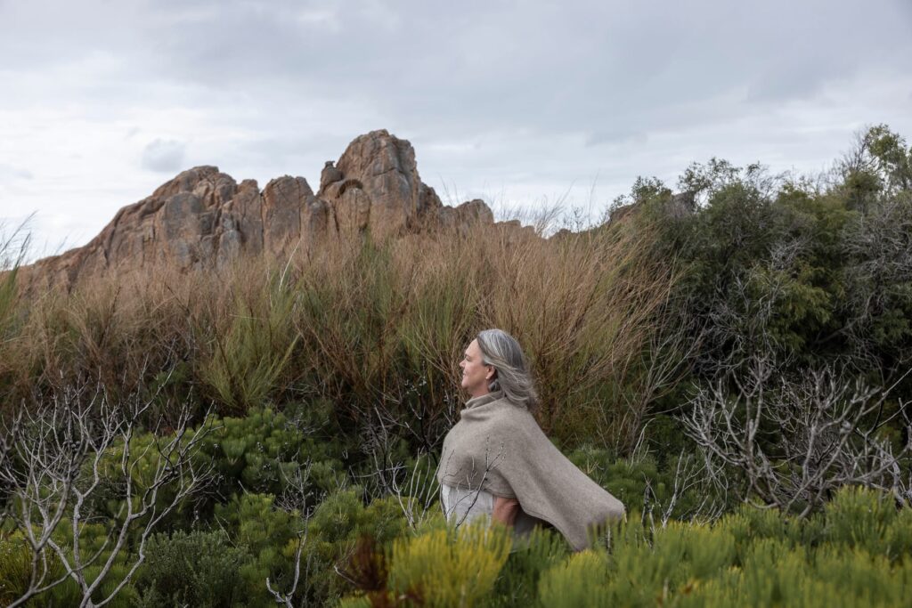 Woman in a sandy coloured shawl standing in nature on an overcast day.
