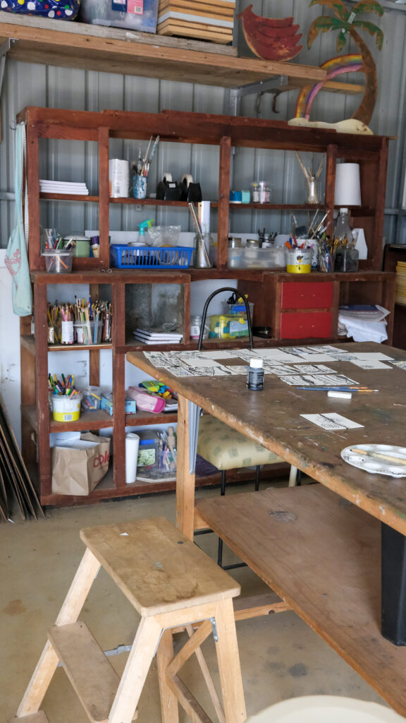 An art studio in a shed, featuring a workshop bench and a shelf of art supplies.
