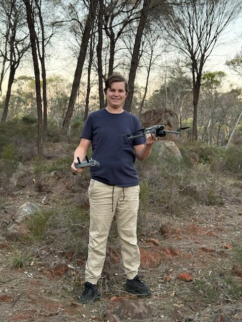 Man standing in bushland holding a drone and controller.