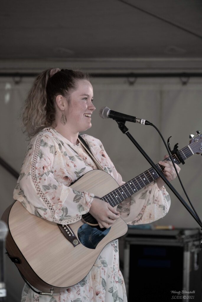 Woman playing the acoustic guitar and singing into a standing microphone.