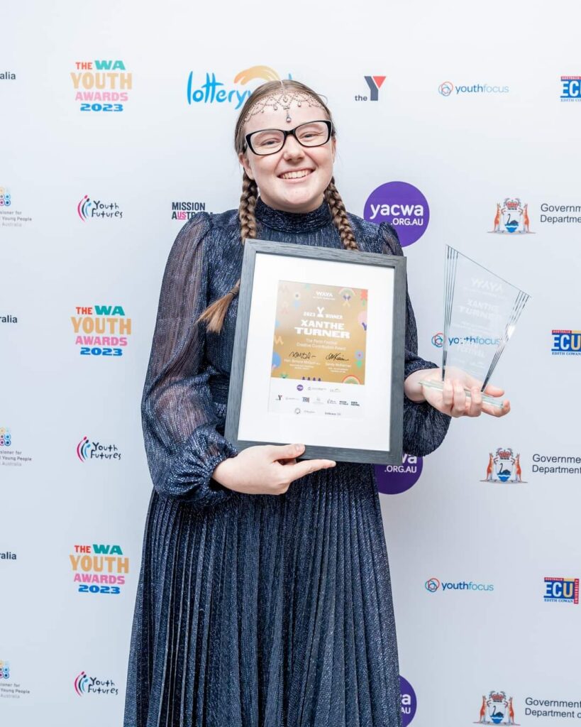 Woman standing in front of a step-and-repeat wall, holding a framed certificate and an acrylic trophy.