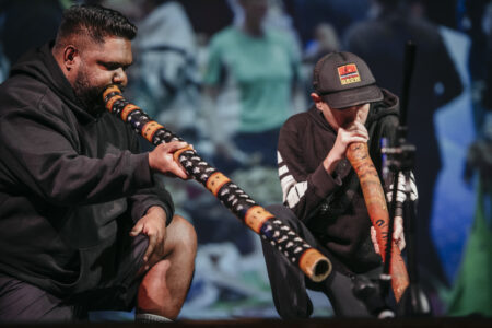 Two men on stage playing the didgeridoo.