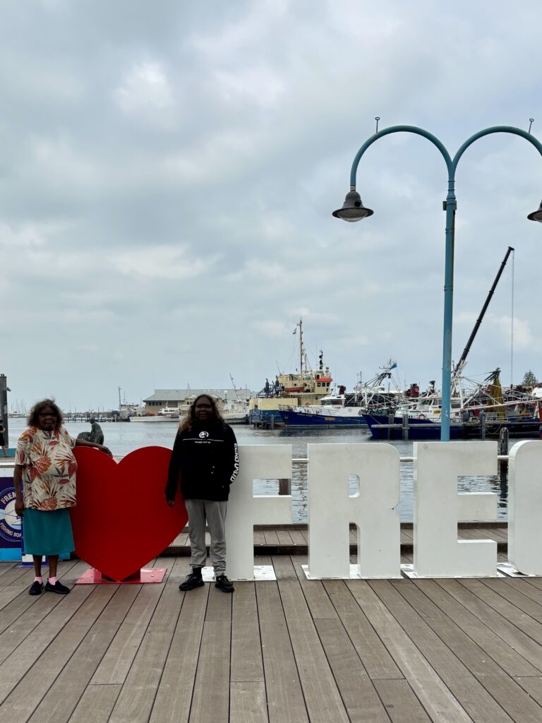 Two women standing on a dock in front of a love heart sign.