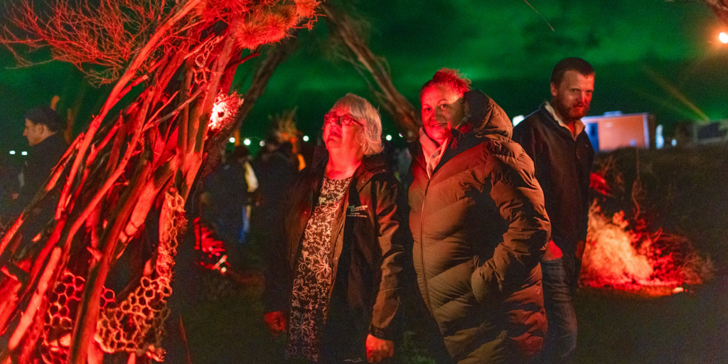 Two people looking at an outside art installation at night, illuminated by red lights.