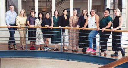 A group shot of a row of people posing on an interior balcony.
